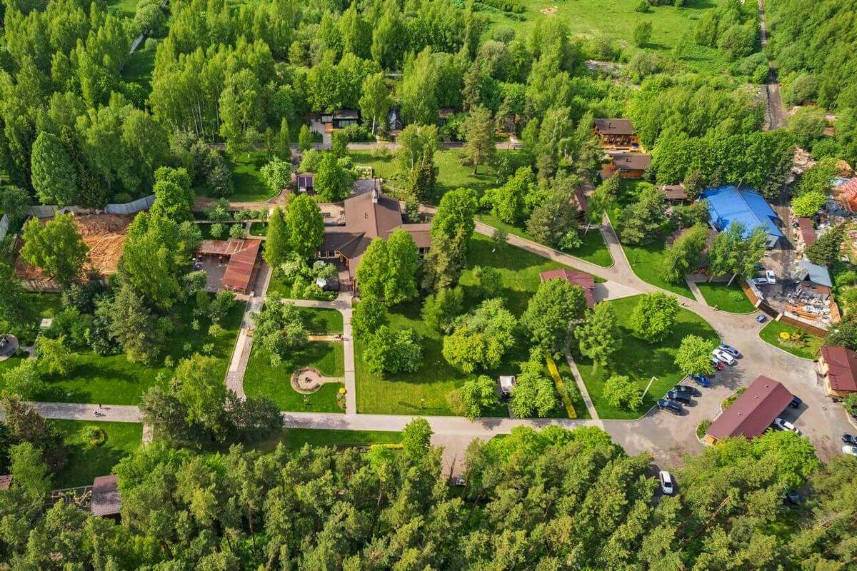 Панорамный вид: лес, дорожки и крыши домиков.